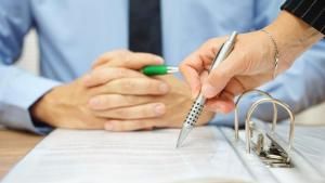 Women pointing pen on page Infront on man sitting with hands folded