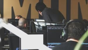 Photo of an office space with multiple workers using their monitors, with a supervisor looking over an employee&#039;s work